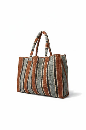 The GABRIELE FRANTZEN Raffia Weekender Bag Tobacco is a large, handmade bag with two handles and vertical stripes in brown, tan, cream, and gray for a textured, artisanal look.