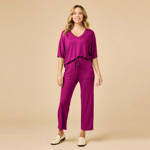 A woman wears a SOFTIES - DREAM RELAXED V-NECK WITH CAPRI LOUNGE SET in magenta, featuring a V-neck top with elbow-length sleeves and matching cropped drawstring pants, paired with cream-colored loafers.