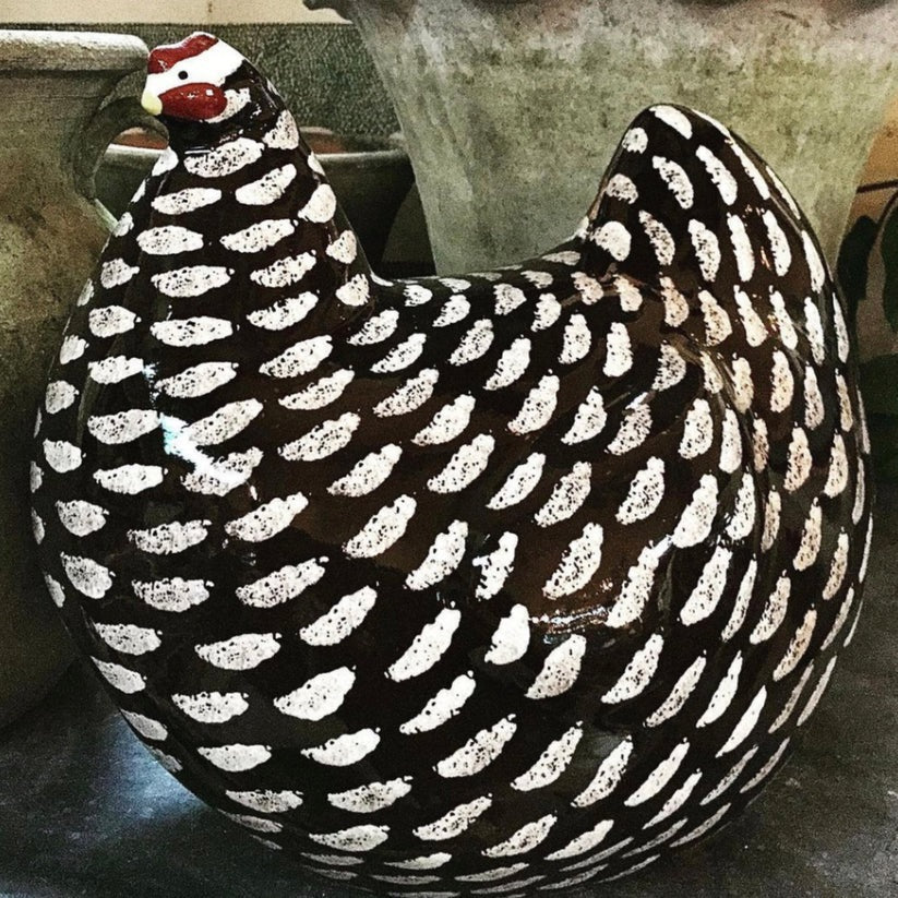 A LES CERAMIQUES DE LUSSAN large ceramic French pullet in black spotted white stands on a light-colored cylindrical base against a plain background.