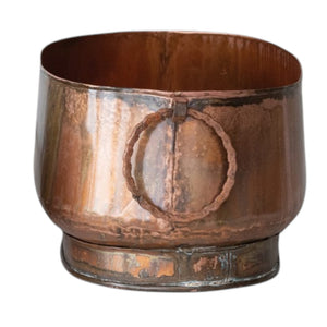 The CREATIVE COOP OVAL METAL PLANTER WITH RING HANDLES, LARGE holds books and dried plants on a light cloth next to a matching cup, set against a plain light wall for charming farmhouse décor.