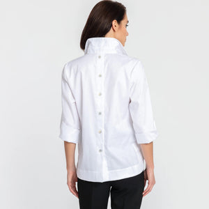A woman with short dark hair models the HINSON WU - AILEEN 3/4 SLEEVE POLISHED COTTON SHIRT in navy, featuring a collared neckline, stretch fabric, and three buttons. She pairs it with white pants and poses against a plain light gray background.