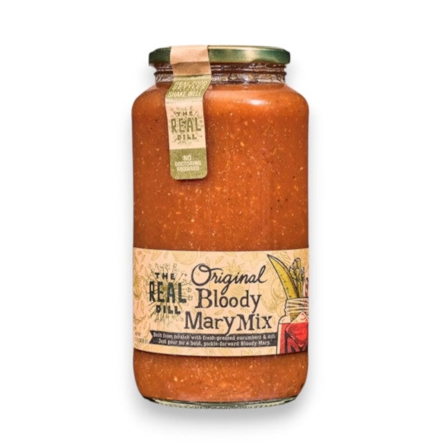 A 32oz jar of THE REAL DILL - ORIGINAL BLOODY MARY MIX by THE REAL DILL is displayed in a sunlit kitchen, surrounded by fresh tomatoes, cucumbers, dill, garlic, and a classic Bloody Mary cocktail.