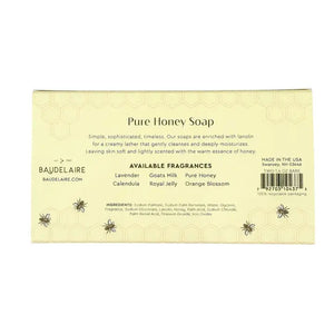 Two BAUDELAIRE soap boxes with floral designs, one opened to reveal a honeycomb patterned soap bar inside. Labels show 'Pure Honey' and 'Royal Jelly'. Text on the side reads "Crafted by Artisans. Cherished by You." The BAUDELAIRE - PURE HONEY SOAP 1.4OZ MATCHBOX DUO is the perfect gift for any occasion. Background is plain white.
