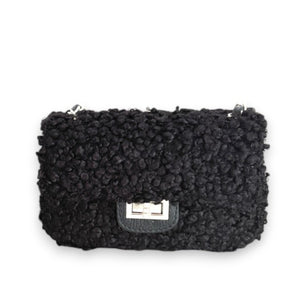 Introducing the VICARIO CINQUE - Brescia Handbag in Black by VICARIO CINQUE, featuring a bouclé exterior that evokes the look of curly wool. This elegant handbag is distinguished by its silver chain strap and rectangular silver clasp on the flap—an ideal accessory to infuse any outfit with a touch of Italian style.