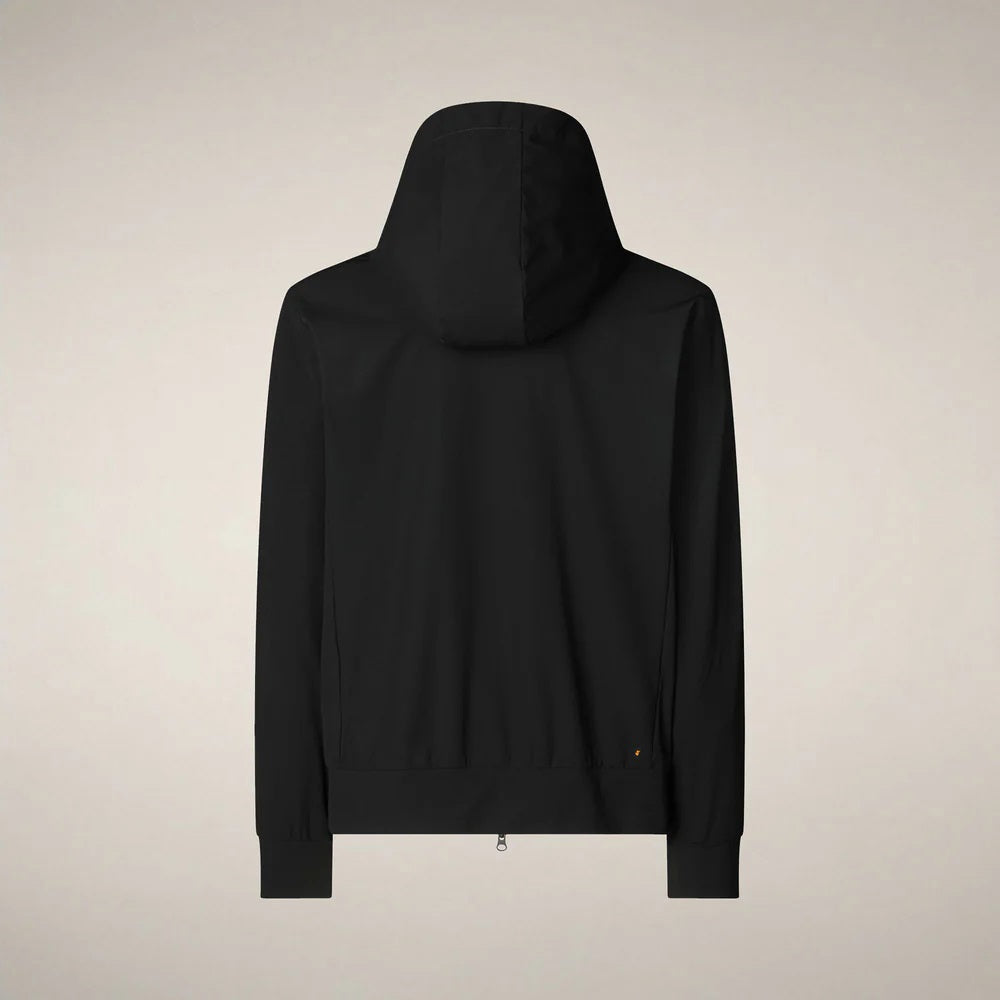 A man faces forward in the SAVE THE DUCK - LUIZ Hooded Jacket in Blue Black from SAVE THE DUCK, paired with black pants and white sneakers, set against a plain beige background.