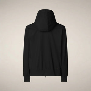 A man faces forward in the SAVE THE DUCK - LUIZ Hooded Jacket in Blue Black from SAVE THE DUCK, paired with black pants and white sneakers, set against a plain beige background.