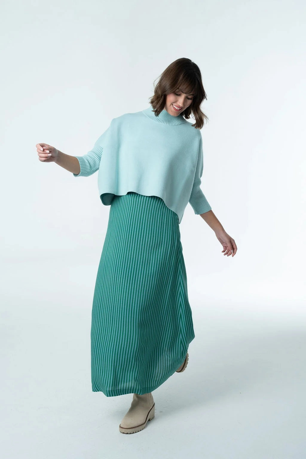 A person wears a light blue cropped turtleneck sweater with a BRITON COURT - TIFFANY MIDI SKIRT IN EMERALD STRIPE and beige ankle boots.