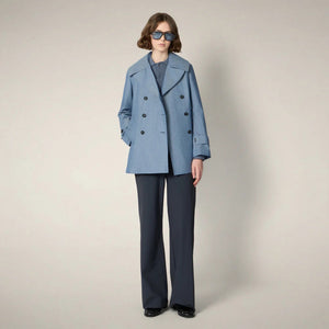 A person wearing dark sunglasses, the SAVE THE DUCK SELA Peacoat Raincoat in Chambray, and wide-leg dark pants stands against a plain light background.