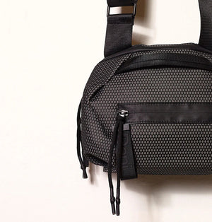 A person in a light beige suit carries the DANIELLA LEHAVI - BONNIE TRAVEL CROSSBODY, a large brown vegan bag with black zipper and strap, shown from shoulders to mid-thigh against a plain background.