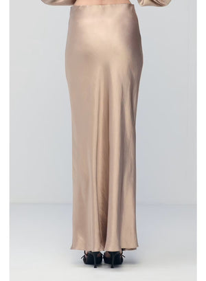 A person wearing the MILVA MI - LONG SATIN SKIRT IN SAND by MILVA, paired with pointed black shoes and standing against a plain, light background.