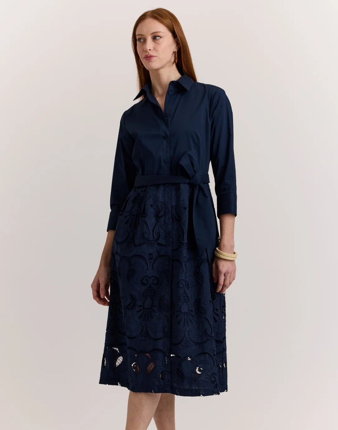 A woman stands against a plain light background wearing the HINSON WU Robin 3/4 Sleeve Eyelet Embroidery Dress in navy, featuring a collared neckline, belted waist, and an elegantly detailed lace-patterned skirt.
