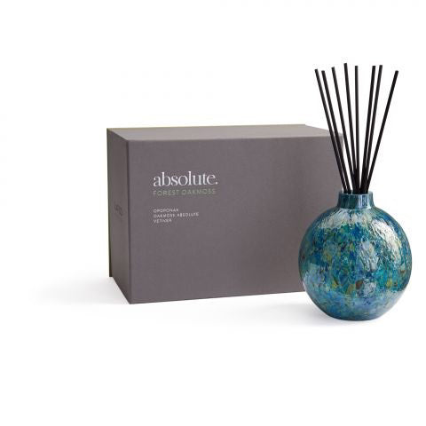 A decorative blue glass diffuser with black reeds, elegantly positioned next to a grey box labeled &quot;LAFCO - Forest Oakmoss Absolute Diffuser,&quot; evokes the enchanting allure of Balkan forests with a hint of violet leaf.