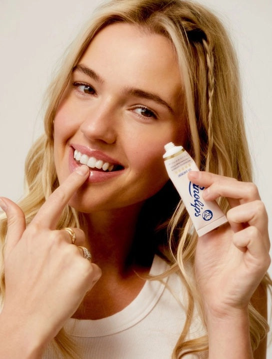 A pink tube labeled “LANOLIPS - 101 OINTMENT MULTIPURPOSE SUPERBALM” from LANOLIPS—an ultra-hydrating moisturizer—displays a blue logo with a sheep’s head and five gold stars, standing upright on a white background.