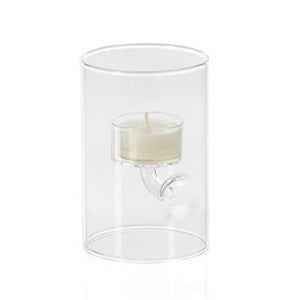 ZODAX SUSPENDED GLASS TEALIGHT HOLDER - EXTRA SMALL displays red tealights burning in clear glass holders of varying heights, set on a white surface with pine branches, berries, and a pinecone against a deep red background.