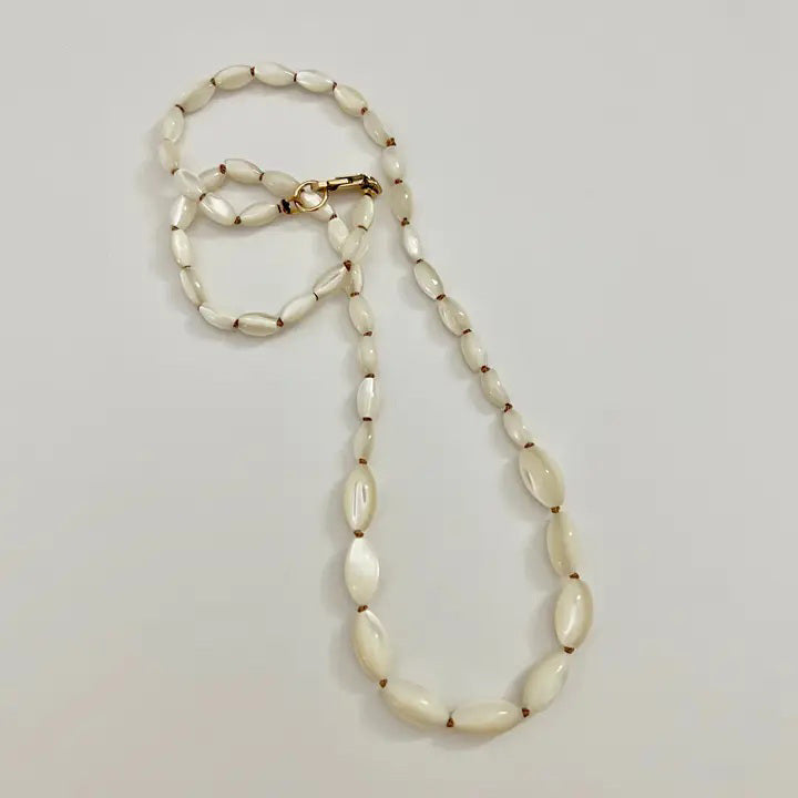 The SANDRINE FRANCE STUDIO - GIANNA NECKLACE features handmade oval white beads, reminiscent of hand-knotted shells, separated by small gold spacers and displayed in a loose curve on a plain white background.