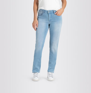 A person is standing against a plain background wearing MAC's DREAM STRAIGHT LEG DENIM jeans in light blue, paired with a white shirt and white sneakers. Their right hand is in their pocket while their left hand hangs down by their side. The slim fit of the MAC jeans provides a subtle shaping effect for a tailored look.
