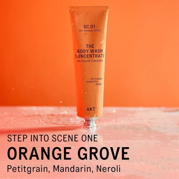 An orange tube of AKT LONDON’s BODY WASH CONCENTRATE ORANGE GROVE is squeezed onto a hand. Beside it, on an orange background, text reads: “SKIN-BALANCING,” “MOISTURE-LOCKING,” “NOURISHING.”.