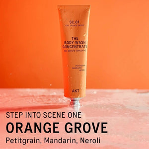 An orange tube of AKT LONDON’s BODY WASH CONCENTRATE ORANGE GROVE is squeezed onto a hand. Beside it, on an orange background, text reads: “SKIN-BALANCING,” “MOISTURE-LOCKING,” “NOURISHING.”.