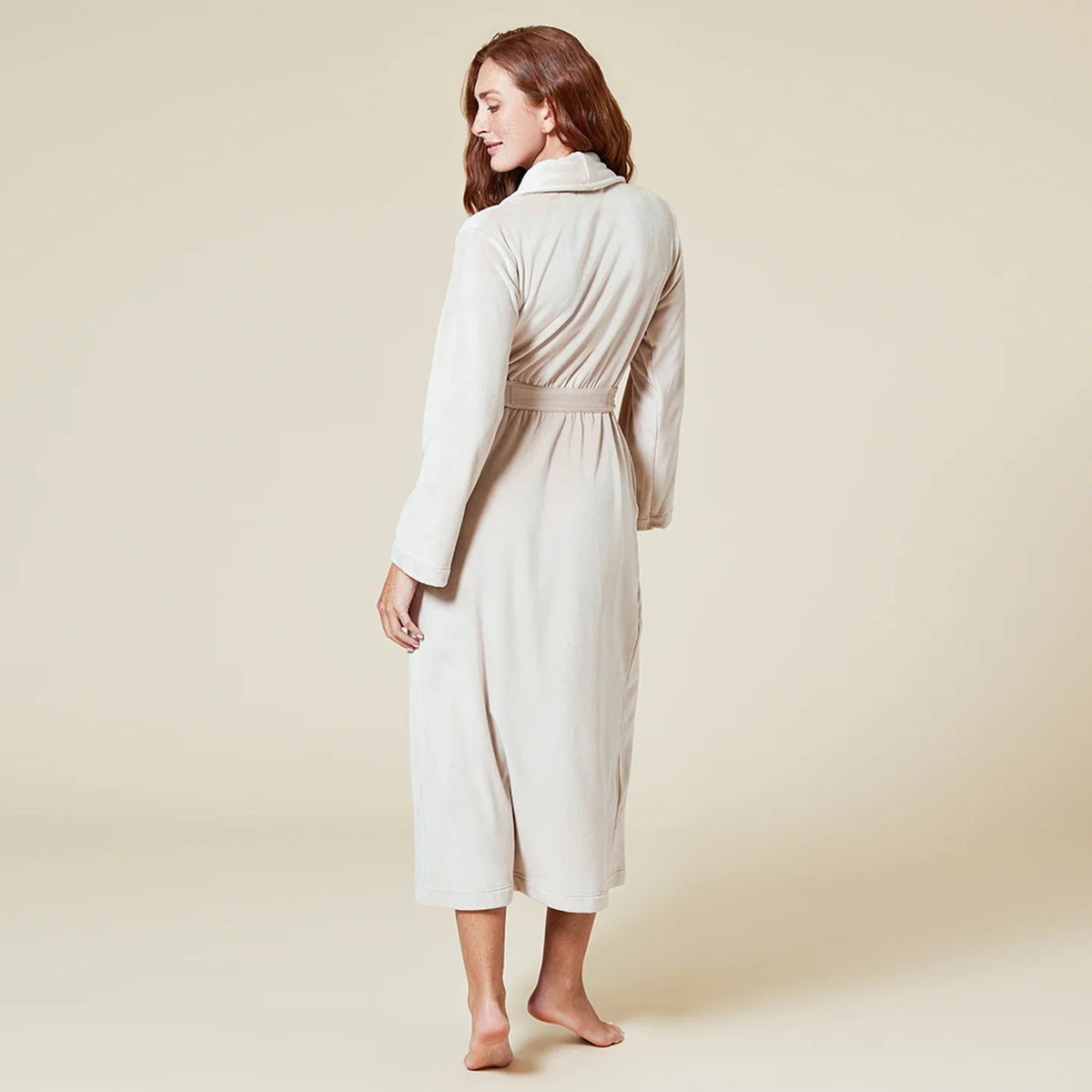 A person wearing a beige SOFTIES - SERENITY WRAP ROBE featuring a wrap silhouette with a tie waist and side pockets.