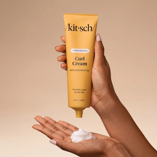 A yellow tube of KITSCH - MOISTURIZING CURL CREAM, formulated with coconut oil and designed for kinky, curly, and coily hair. This KITSCH brand curl cream is labeled as moisturizing and ideal for frizz control, with a smear of the product shown behind the tube.
