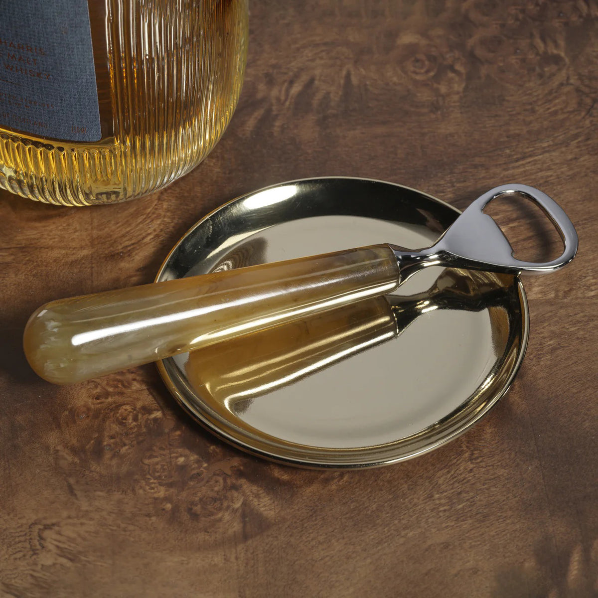 The SPIGA BOTTLE OPENER by ZODAX, featuring a brass resin head and smooth amber-colored handle, rests on a white surface—showcasing its elegant design and unique materials.