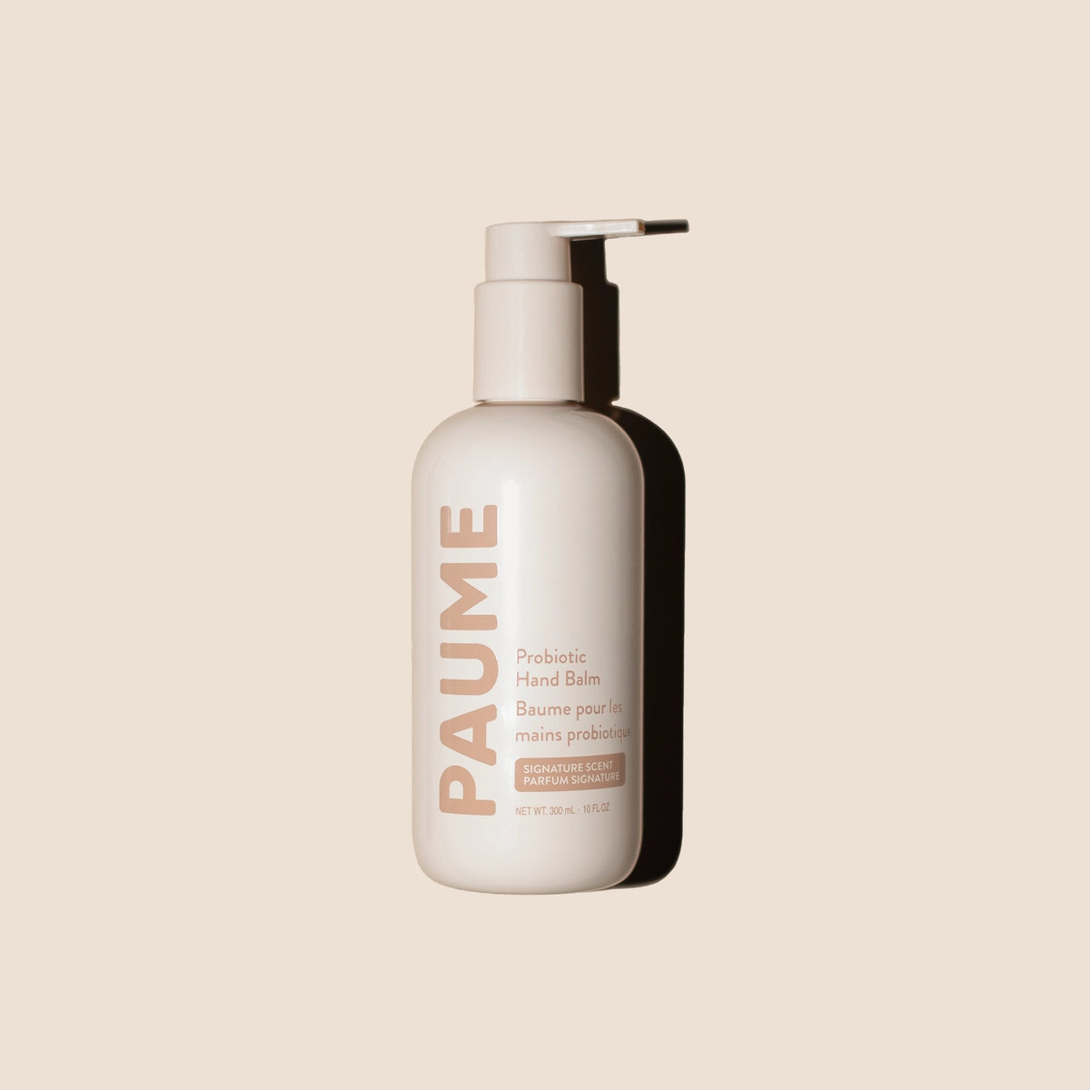 A beige pump bottle labeled "PAUME - PROBIOTIC HAND BALM 10OZ" by PAUME, featuring plant-based emollients, stands upright on a light beige background with a right-cast shadow. The label shows English and French text and a net weight of 10oz.