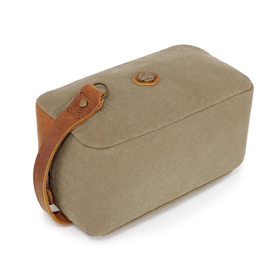 The TSD BRAND Valley Oak Toiletry Bag in olive is a rectangular, handcrafted travel essential made from durable canvas, featuring a tan leather strap and a small leather patch for added style.