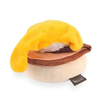 Introducing the PLAY PET LIFESTYLES/BRANDS BARKING BRUNCH - BENNY’S BENEDICT: an adorable dog toy designed to look like a plush egg with a yellow yolk atop a round, brown base, mimicking a classic brunch favorite. Perfect for playful pups, this fun and charming brunch-themed toy features a black fabric tag attached at the bottom.