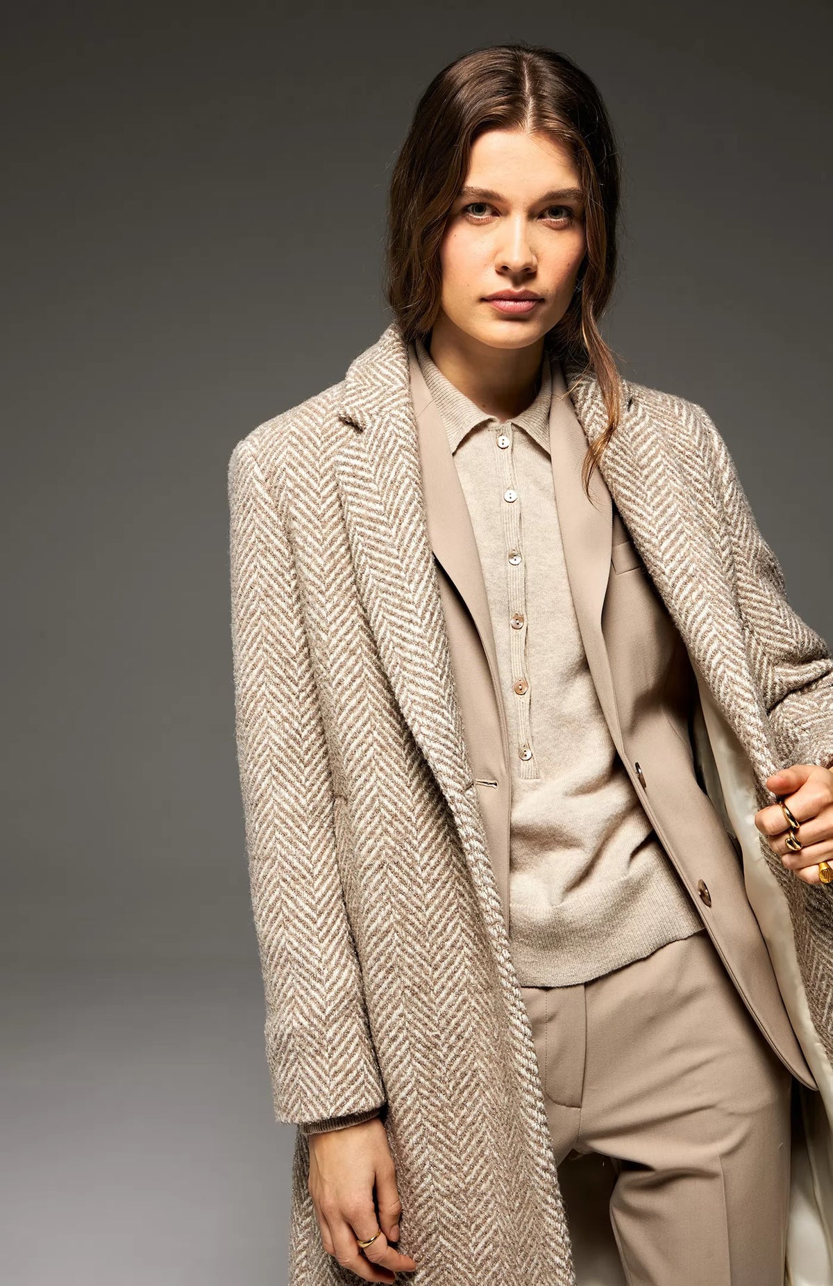 A sophisticated, single-breasted coat designed in a macro herringbone pattern on a white background. This SEVENTY coat, known as the SEVENTY - SINGLE BREASTED LUREZ MACRO HERRINGBONE COAT, features a notched lapel collar, long sleeves, and two buttons for closure. It’s crafted in light grey and white hues and proudly made in Italy with a label inside the collar that reads &quot;Sustain.