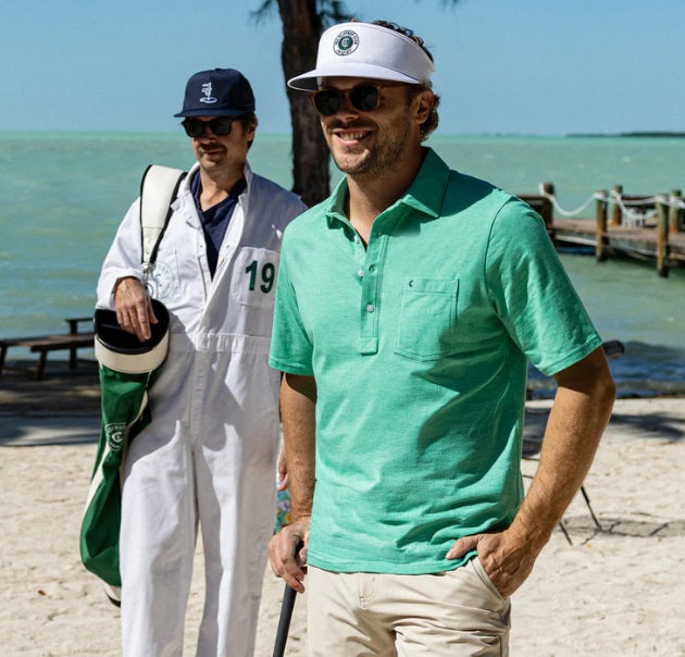 A person wears the CRIQUET Top-Shelf Players Shirt in Golf Green Microstripe with white buttons and a front pocket displaying a small embroidered logo; their face is partially out of frame.