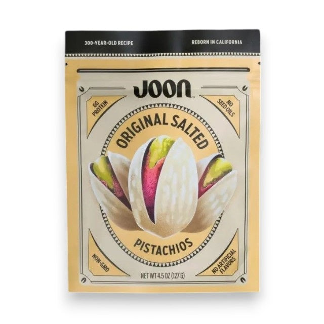 A bag of JOON Original Salted Pistachios, a distinguished offering from the JOON brand, rests on a dark surface with several shelled and unshelled pistachios scattered around. The packaging emphasizes “No GMOs” and “No Artificial Flavors,” underscoring these premium nuts as an irresistible gourmet snack.