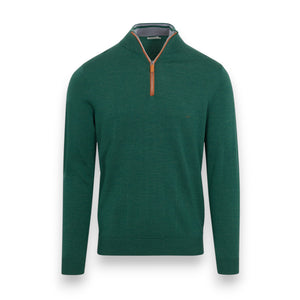 A man in white pants stands before a large fallen tree in the forest, wearing the COLLARS AND CO Hunter Green with Brown Suede Trim Cashmere Touch Australian Merino Wool Sweater, with one hand in his pocket and a brown leather backpack by his side.