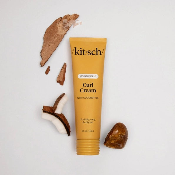 A yellow tube of KITSCH - MOISTURIZING CURL CREAM, formulated with coconut oil and designed for kinky, curly, and coily hair. This KITSCH brand curl cream is labeled as moisturizing and ideal for frizz control, with a smear of the product shown behind the tube.