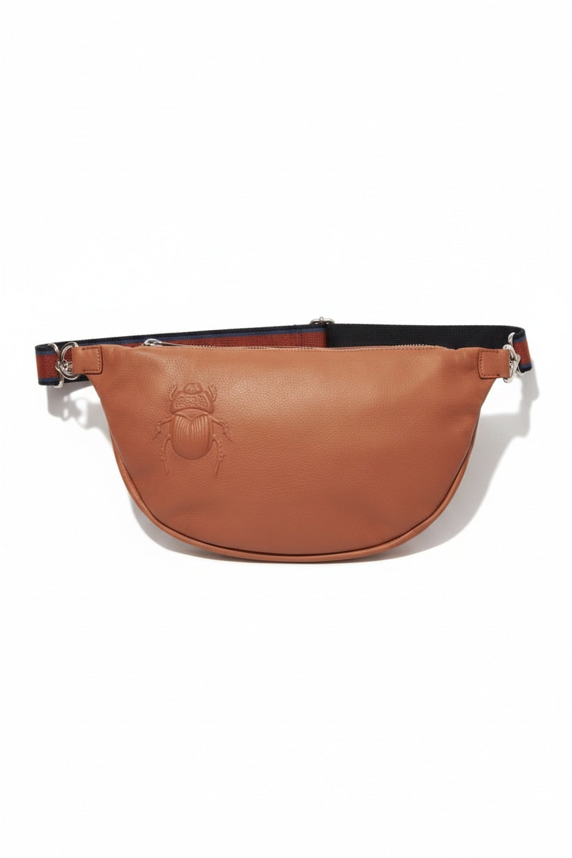 The GABRIELE FRANTZEN - SCARAB XL Leather Beltbag in Cognac features a brown Italian leather construction with an embossed scarab beetle design on the front, complemented by a black adjustable crossbody strap and silver hardware. The bag is displayed against a plain white background.