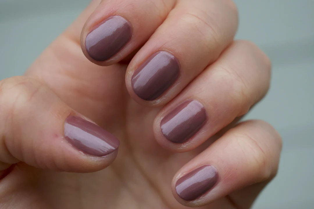 A glass bottle of TENOVERTEN - NAIL POLISH from the brand TEN OVER TEN, featuring a white cap and a dusty pink nail color. The front label displays "TEN OVER TEN" in white uppercase letters. This vegan, eight-free formula ensures both beauty and peace of mind. The background is plain and light-colored.