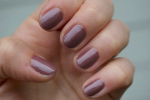 A glass bottle of TENOVERTEN - NAIL POLISH from the brand TEN OVER TEN, featuring a white cap and a dusty pink nail color. The front label displays "TEN OVER TEN" in white uppercase letters. This vegan, eight-free formula ensures both beauty and peace of mind. The background is plain and light-colored.