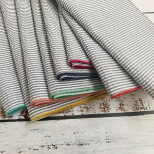 A set of DOT AND ARMY - GREY SEERSUCKER DINNER NAPKINS, each with colorful edging, is fanned out on a white background.