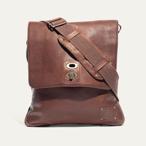 The WILL LEATHER GOODS - OTTO CROSSBODY BAG IN COGNAC, a full-grain leather bag with plaid lining, is shown open from above holding a camera, book, and wallet.