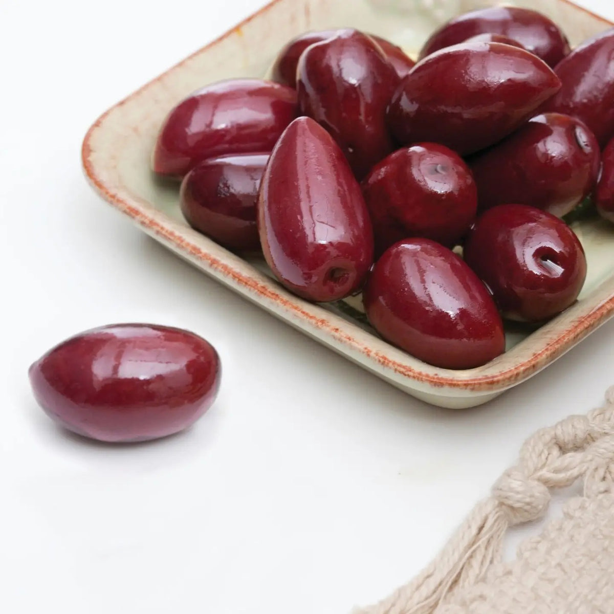 A clear glass jar of DIVINA - KALAMATA OLIVES from Greece, with a purple label and black lid, filled with plump, dark Greek olives.