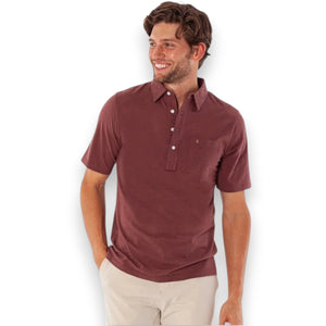 A man wearing the CRIQUET Top-Shelf Players Shirt in Mudslide Microstripe and beige pants stands with one hand in his pocket, smiling and looking to his left.