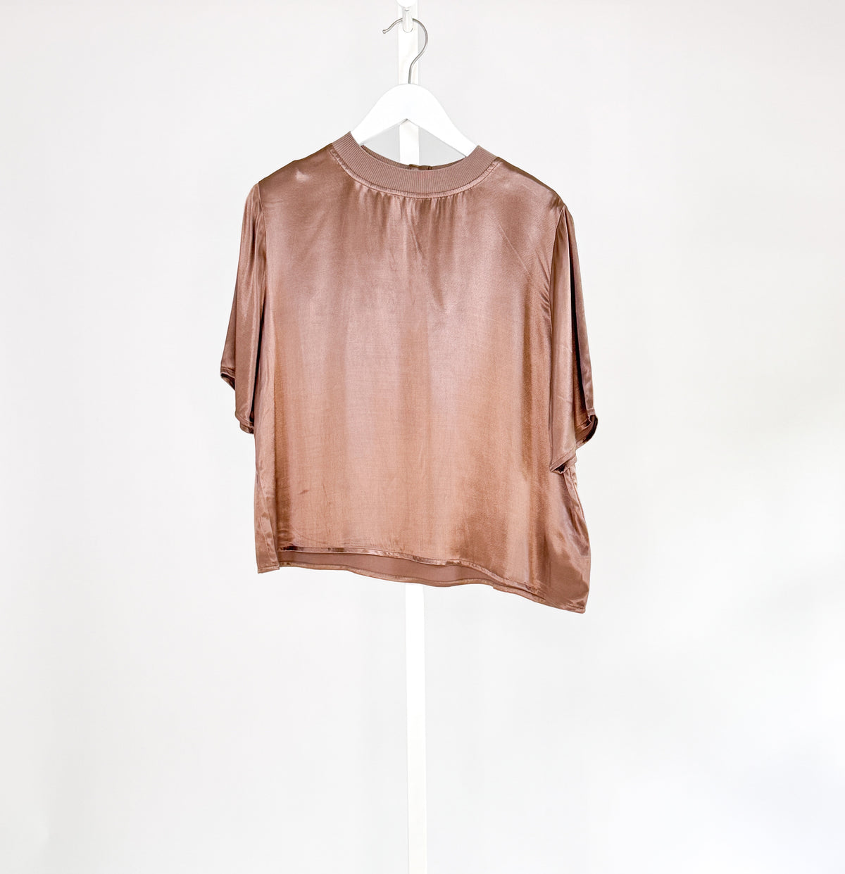 A shiny ROSE &amp; CROWN - SATIN CREW NECK TEE in rose gold hangs on a white hanger against a plain white background, shown from the back with short sleeves.