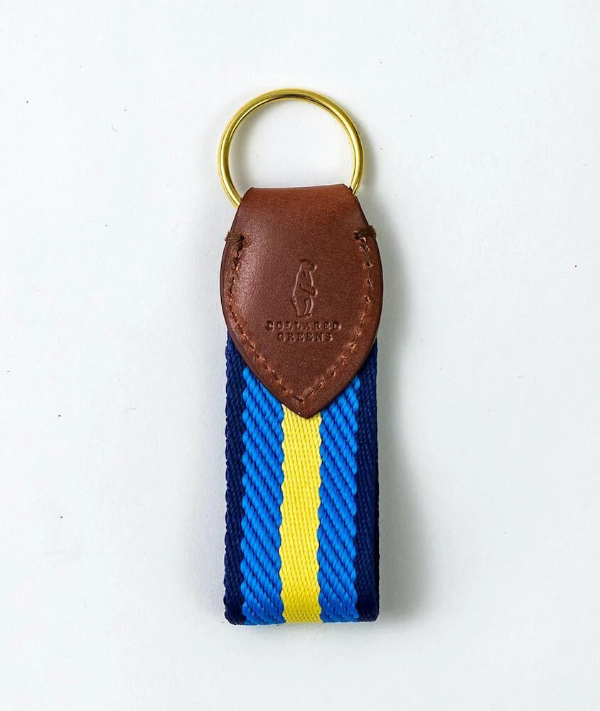 The BIRD DOG BAY COLLARED GREENS Dockside Key Chain features a gold and yellow-blue strap, a brass ring, and a brown leather top embossed with a golfer.