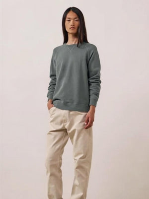 A close-up view of a person wearing the HARTFORD light fleece sweatshirt in charcoal, made in Portugal, featuring a distinctive X-shaped decorative stitch detail at the base of the collar.