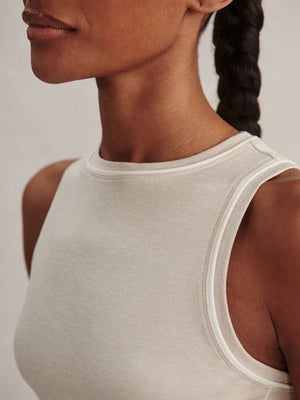 Woman wearing a light gray VARLEY - LETTIE TANK TOP IN PEBBLE MARL, a brown baseball cap, and brown sweatpants tied at the waist with a tote bag over her shoulder.