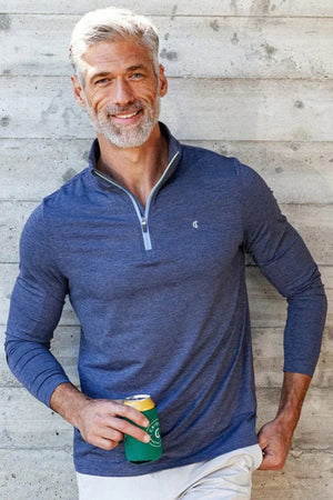 A man wears the CRIQUET FEATHER Performance Knit Quarter Zip Pullover in blue, featuring moisture-wicking fabric, a light blue zipper, and a small chest logo, standing against a plain white background.