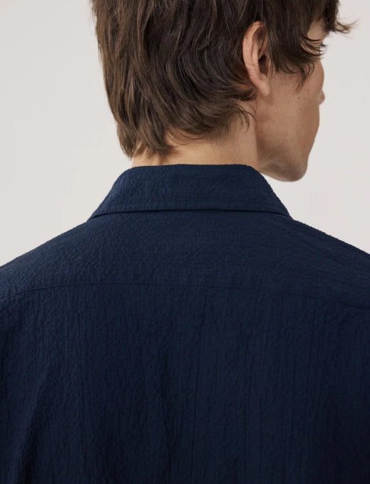 A young man with short brown hair wears the HARTFORD - PEDRO SHIRT IN NAVY and light blue jeans, standing against a plain white background.