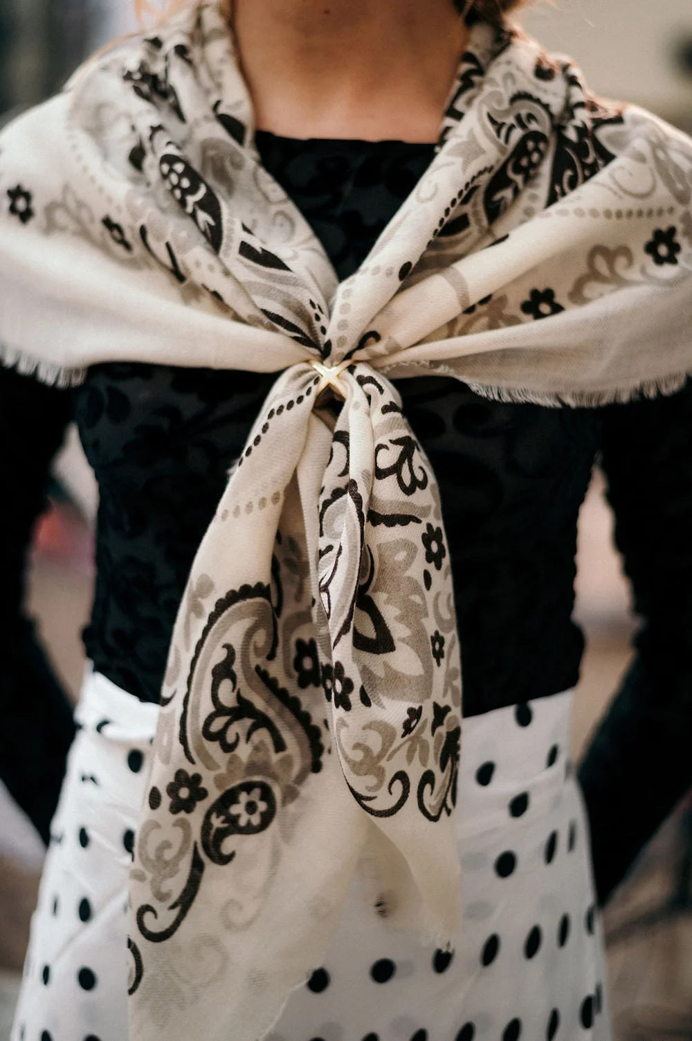 The MAISON LECOMTE - BANDANA SCARF IN ECRU GREY AND BLACK by MAISON LECOMTE FLAMENT features a square silhouette in white, adorned with intricate black and grey paisley and floral motifs. Symmetrical, ornate designs and decorative edge accents combine to evoke classic elegance, while its luxurious wool-cashmere blend ensures exceptional comfort.