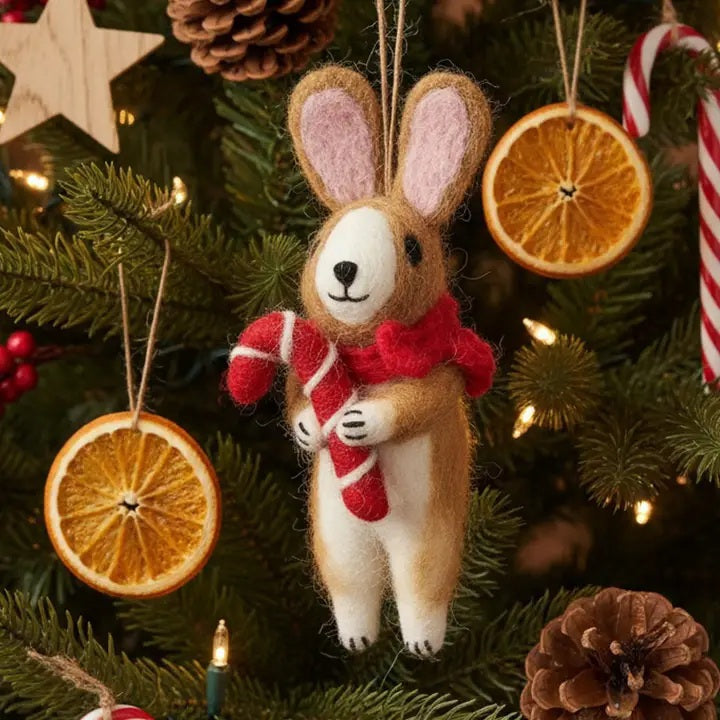 A CINNAMON RABBIT ORNAMENT by FELT SO GOOD hangs on a Christmas tree decorated with a felt rabbit, a candy cane, dried orange slices, and pinecones.