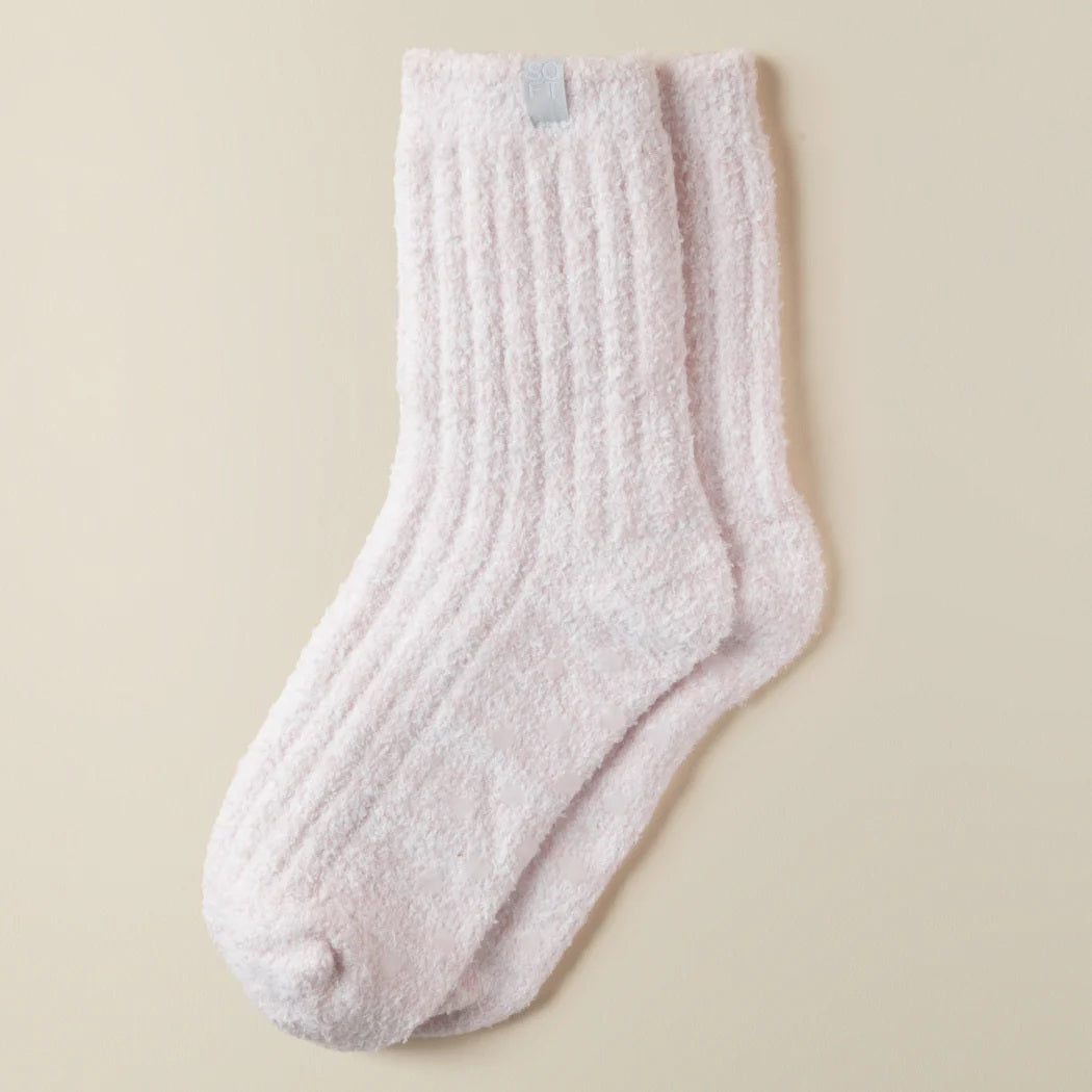 Two feet in SOFTIES - MARSHMALLOW CREW SOCKS IN HEATHER BLUSH PINK are raised against a beige background. These plush SOFTIES socks look cozy and soft, offering warmth and comfort.
