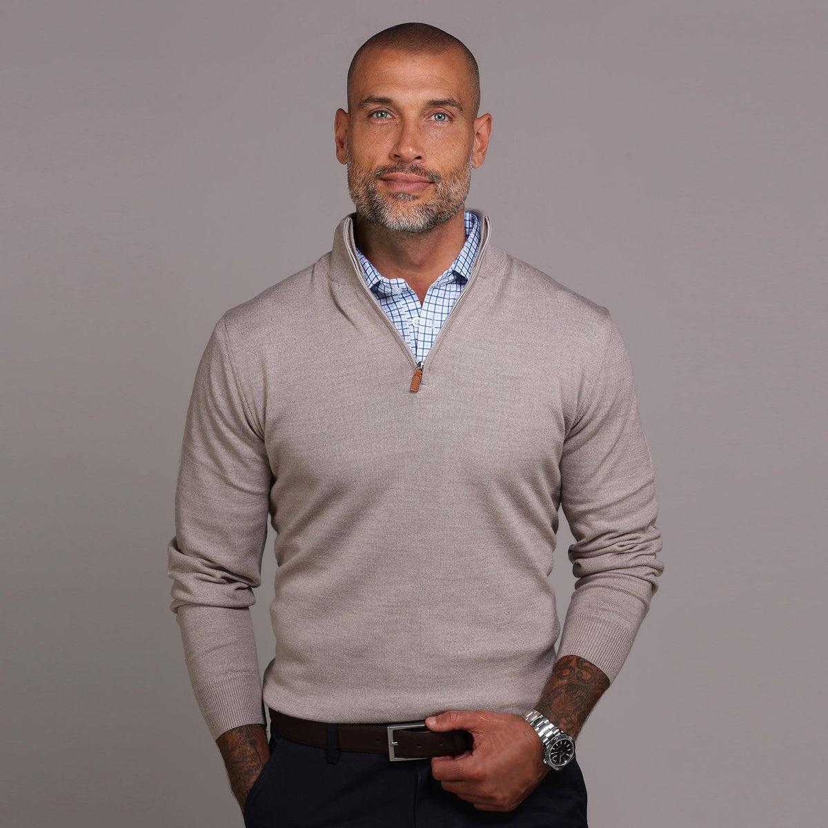 A smiling man with a shaved head and trimmed beard wears the COLLARS AND CO Oatmeal Cashmere Touch Australian Merino Quarter Zip Sweater over a blue checkered shirt, posing against a plain gray background.